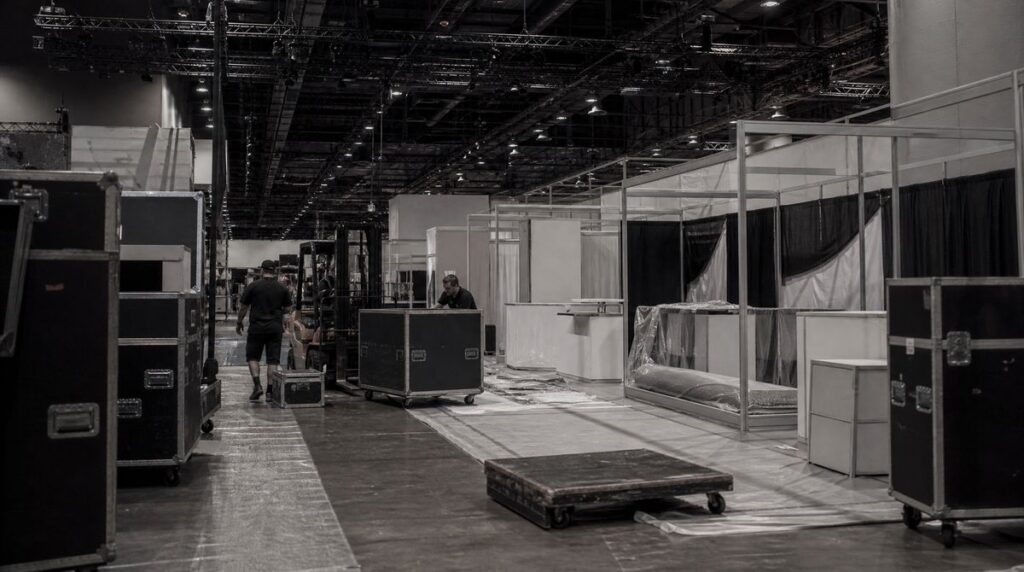 Crew moving road cases past half-built booths on a convention hall floor